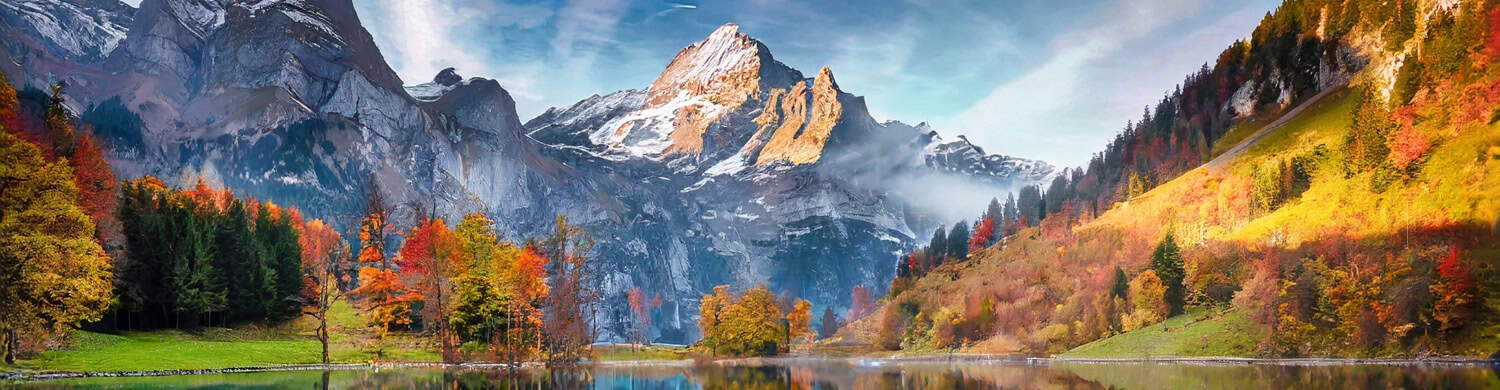 Large Colorado mountain dusted with snow behind a small body of water and several trees in fall colors.